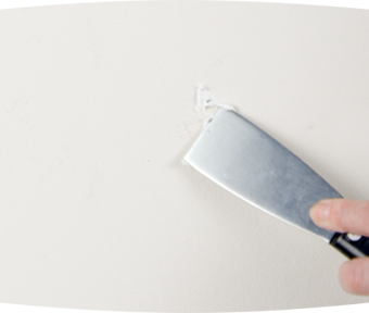 Person using a putty knife to fill a hole with spackle