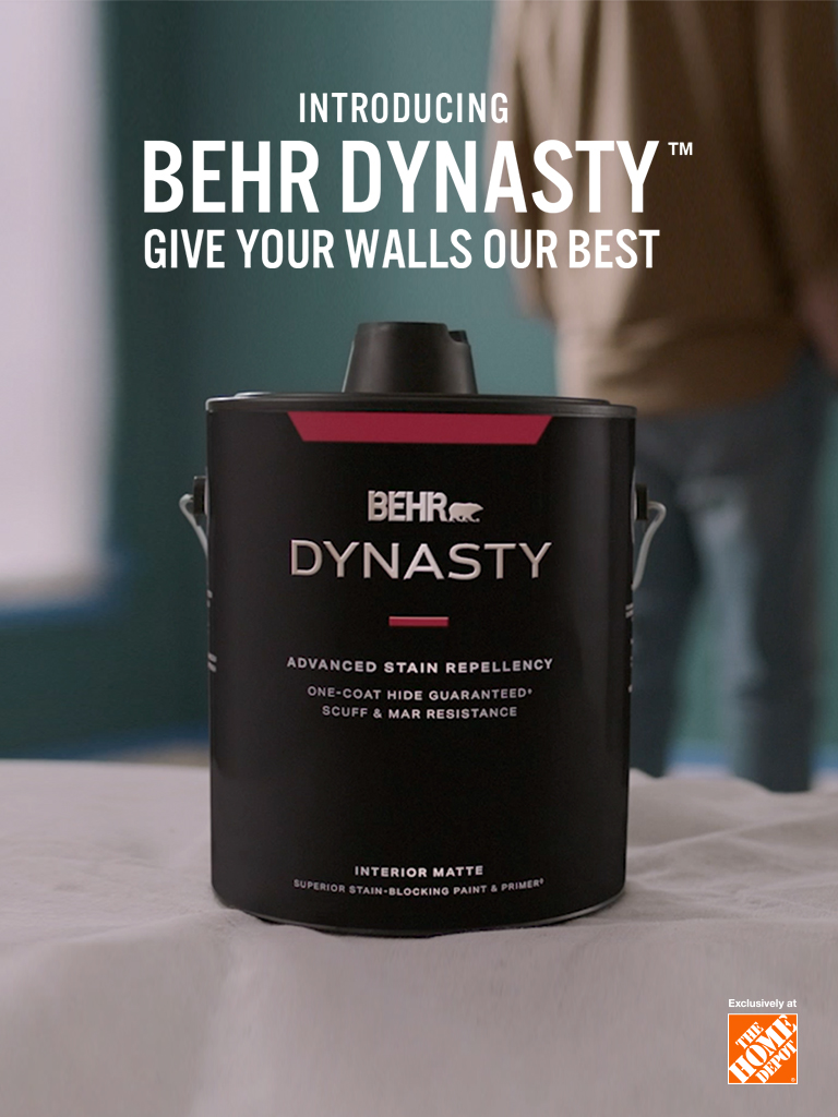 Mobile-sized image of a couple getting ready to paint with a can of BEHR DYNASTY Flat interior paint and the words Introducing BEHR DYNASTY Give Your Walls Our Best in foreground.