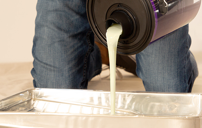 Person pouring paint into a paint tray with the Behr Simple Pour Lid and Spout.