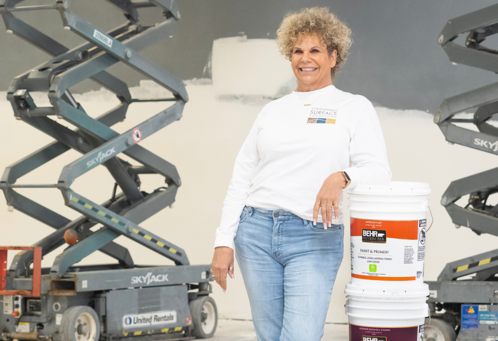 A woman painter leaning against a stack of 5 Gallon Behr Premium Paint
