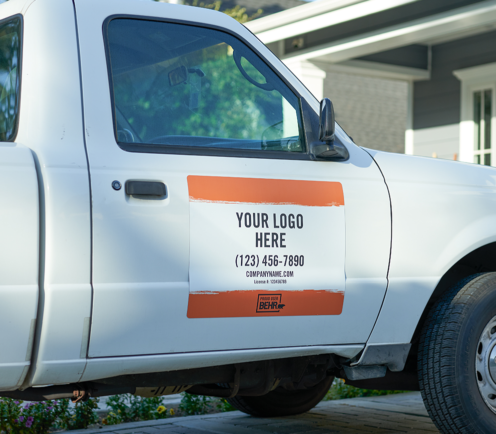 A close up view of a sign that is stuck to a door of a pick up truck. The sign is printed with the words YOUR LOGO HERE - (123) 456-7890 - company.com - PROUD USER BEHR.