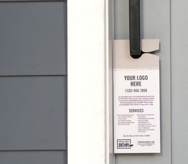 An image of door hanger that is hooked on a front door handle. The door hanger is printed with the words YOUR LOGO HERE - (123) 456-7890 - company.com - PROUD USER BEHR. Along with words you cant read but meant for businesses to put inro and list of services offered.