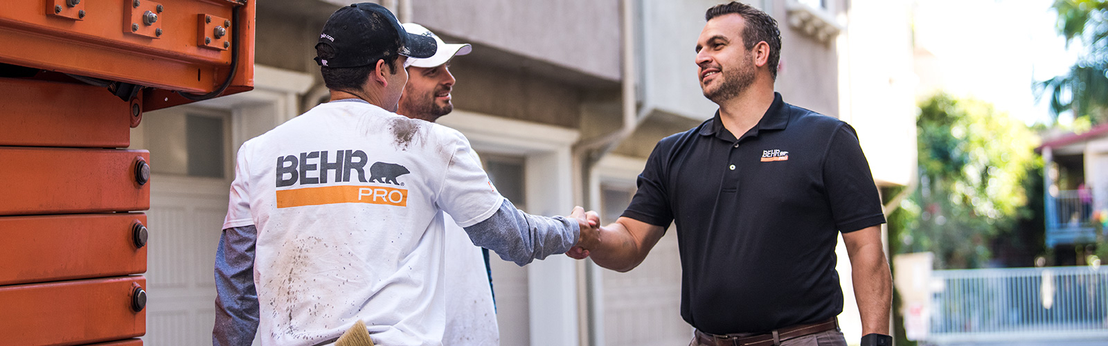A BEHR PRO Rep shaking hands with on of the 2 Pro Painters. In the background is a multi family condo units.