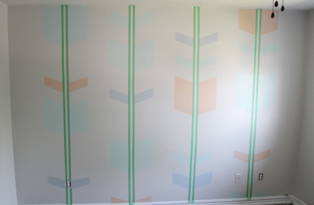wall with partially painted arrow patterns and remaining painters tape still applied