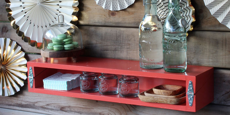 Red shelf attached to a shiplap wall decorated with folded paper fans
