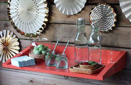 Red shelf in its unfolded position, holding glassware, plates and macarons