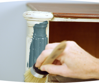 Person painting detailed areas of a dresser with a paint brush