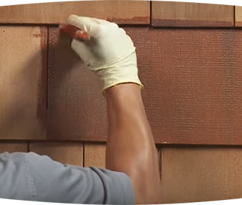 Person staining wood siding with paint brush