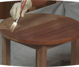 Person staining wood table with small paint brush