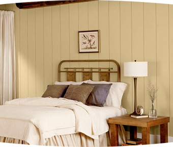 Paneled bedroom with white comforter covered bed and table with lamp on it