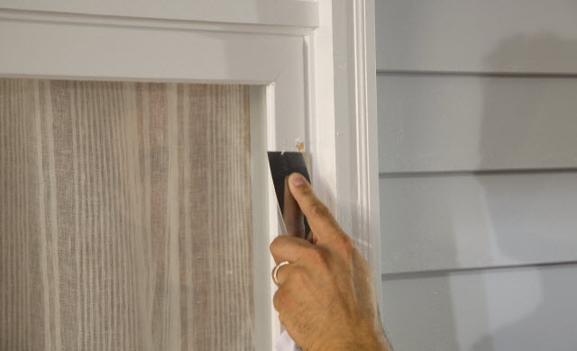 Image demonstrating a person using a tool to peel paint off of a window frame.