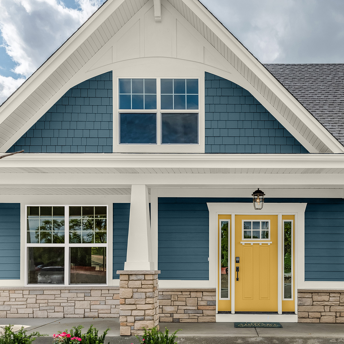 A blue house exterior and yellow door painted with Behr Dynasty Exterior paint