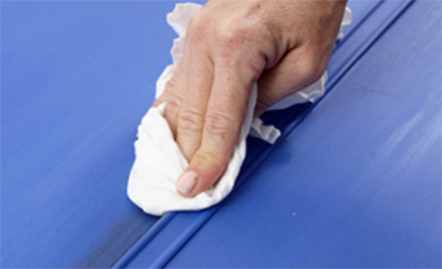 Person's hand using a rag wiping a blue wall