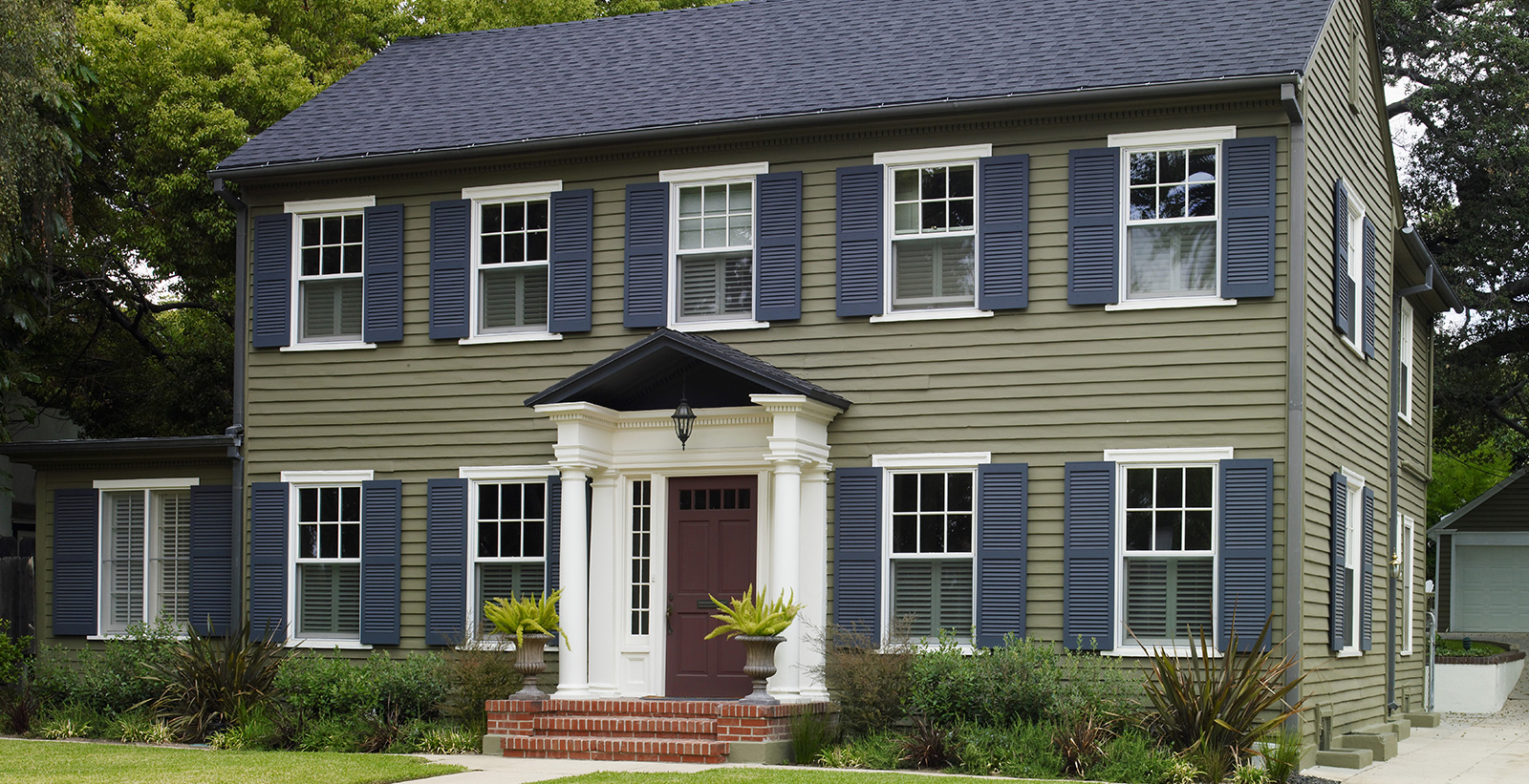 Colonial themed house with green walls, white trim, blue shutters and red door.