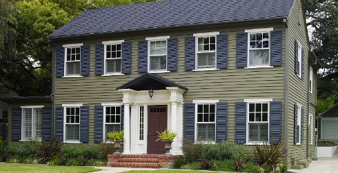 Colonial themed house with green walls, white trim, blue shutters and red door.