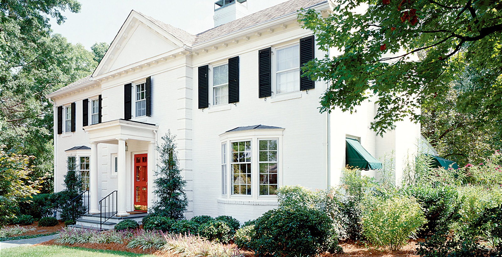 Colonial themed house with white walls, white trim, black shutters, and red door.