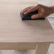 Person sanding a wood table with a sanding block