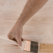 Person applying pre-stain wood conditioner with a paint brush