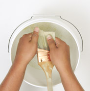 Person cleaning a paint brush in a bucket with soapy water