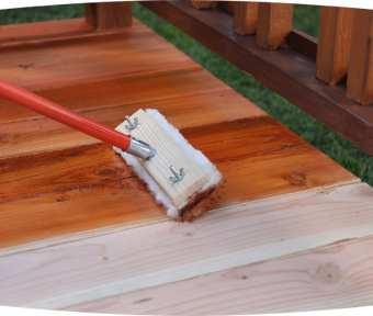 A brush applying stain to a deck