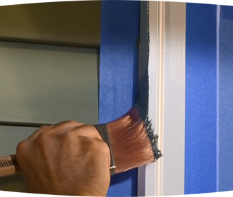Person painting trim of a house with blue tape around it