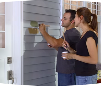 A man and a woman testing paint colors on the outside of a house