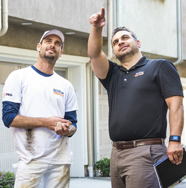 A BEHR PRO Rep pointing at a building while a Pro Painter is looking at what he is pointing.