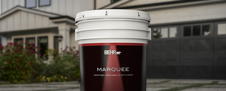 Image of a 5 gallon can shot of BEHR MARQUEE in front of a house.
