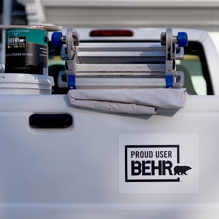 Mobile view of a pick up truck with a Behr sticker that says PROUD USER BEHR. On the back you can see a ladder, dropcloth, 1 gallon of BEHR PREMIUM PLUS Exterior Paint.
