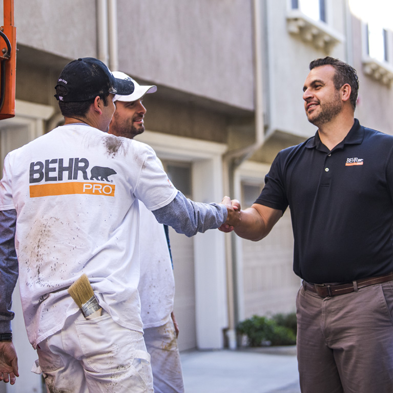 A mobile view of a BEHR PRO Rep shaking hands with on of the 2 Pro Painters. In the background is a multi family condo units.