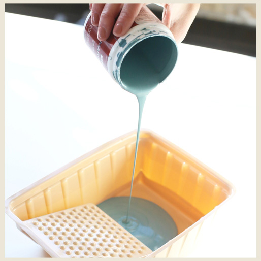 An image showing a person's hand holding a small paint container and pouring paint into a plastic tray.