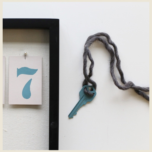 A house key fully painted and dry  with yarn through keyholes.  A shadow box partly showing a pinned down house number.
