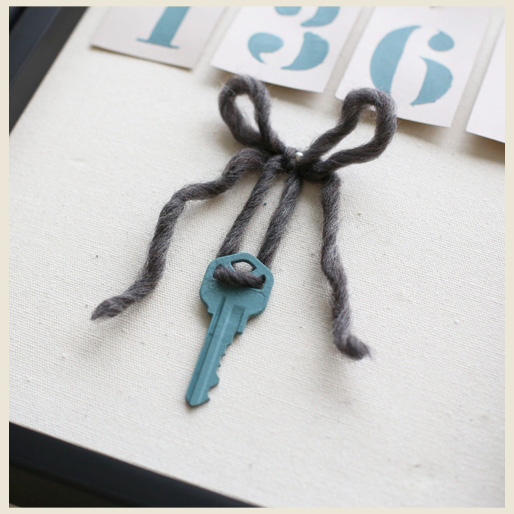 A painted house key and yarn pinned down on shadow box ready for display.