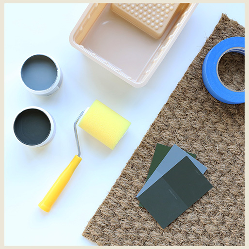 Materials to create a customized jute doormat: jute doormat, paint, roller, tape and plastic tray.