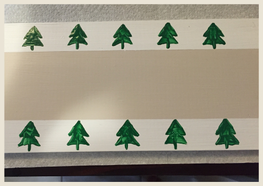 Wood board after being painted with borders and pine tree stencils.