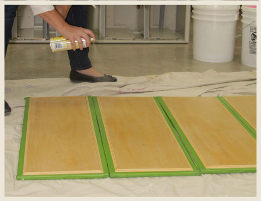 A woman's hand spraying shellac to wood panels.