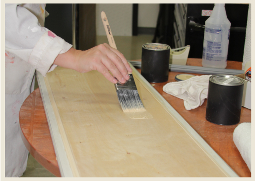 A hand applying wood stain to wood panel.