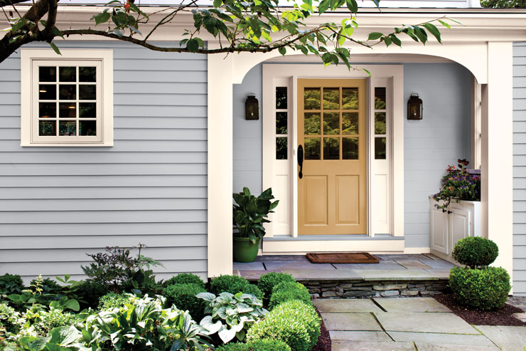 This is an image of a home exterior painted in Classic Silver. The main focus is the accent door painted in Royal Gold M280-4. The home has surrounding greenery with different plants. 