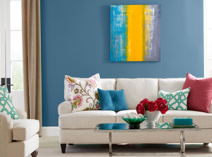 A living room with walls painted in blue. Pillows are solid blue and red, flower pattern and chain pattern.