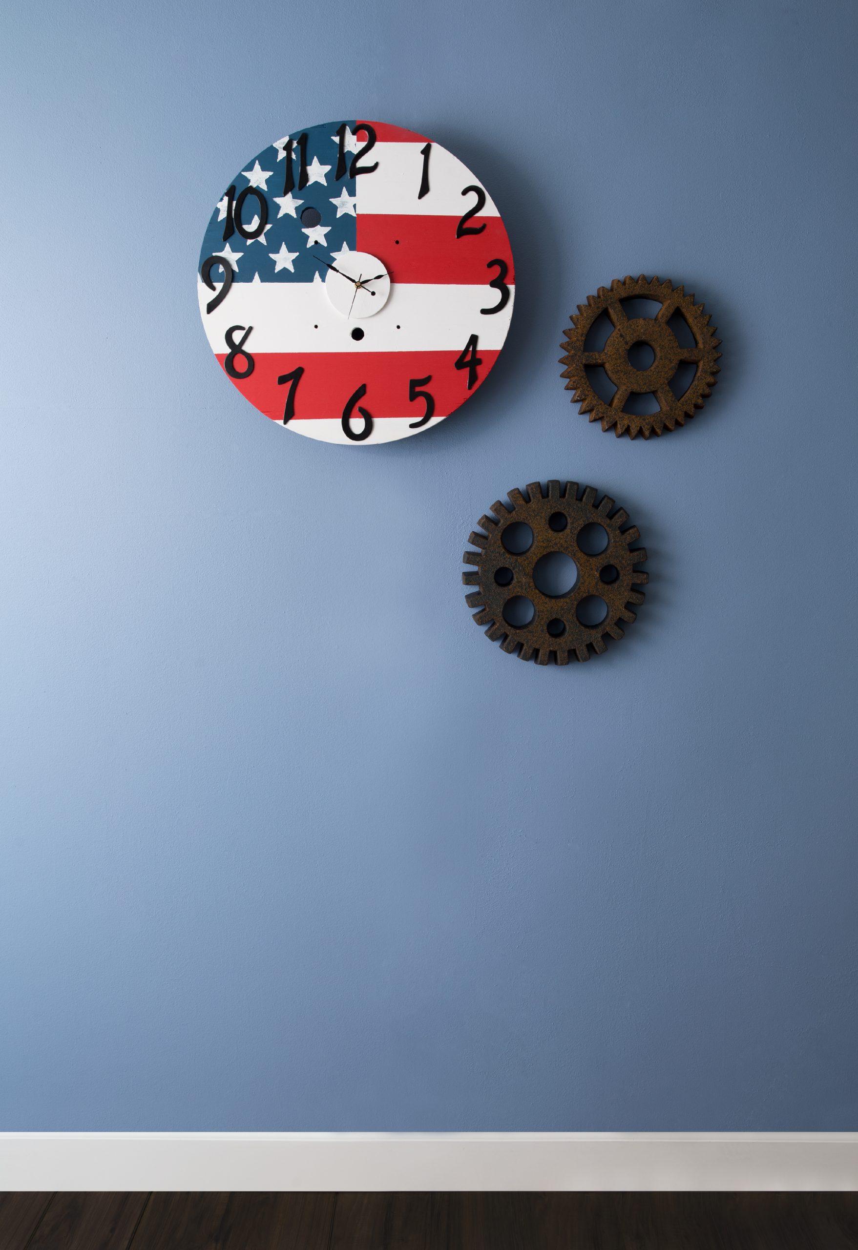 A clock hanging on a blue wall. The clock is painted to look like the patriotic flag.