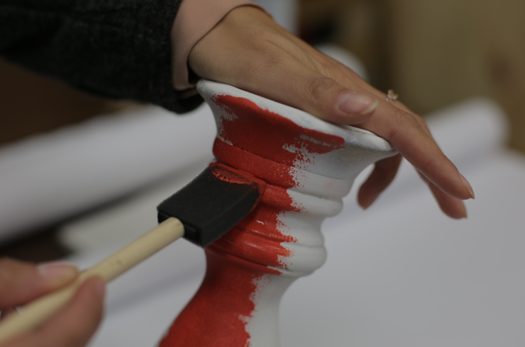 Woman's hands painting wood candlestick with red paint.