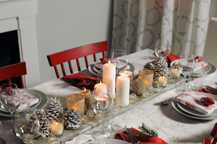 Table runner board centerpiece decorated with lit candles and painted pine cones sitting on a distressed wood plank.