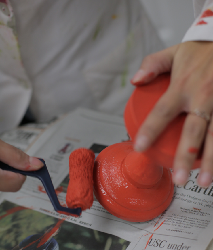 Hands roll painting wood candlestick with a second coat of red paint.
