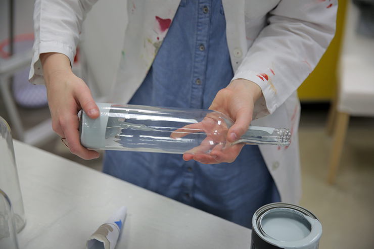 Moving paint around the inside of the tall glass jar to cover it.