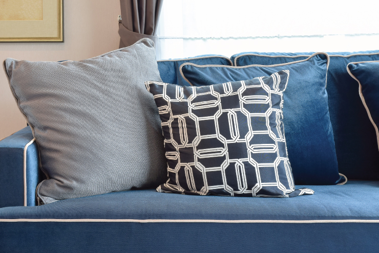 A blue sofa with textured and patterned throw pillows in shades of gray, blue or white.