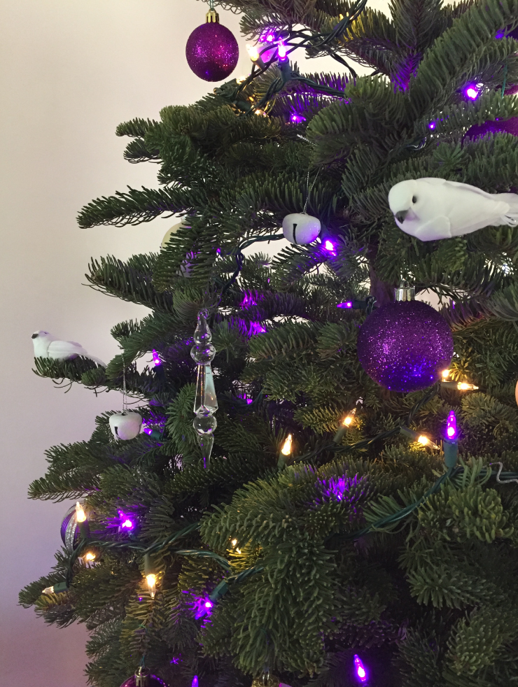 Tight crop of a holiday tree decorated with white doves, and purple lights and bulbs.