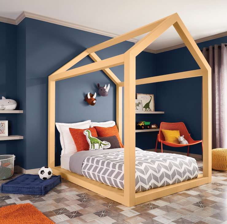 A kid's bedroom featuring dark blue walls and yellow, orange and white accents incorporated in the forms of area rugs, furniture and bedding.