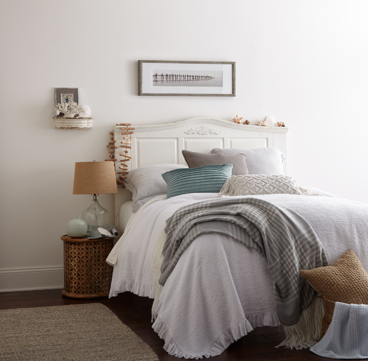 Bedroom with white walls. The bedding is styled with white and grays and a pop of a light blue.