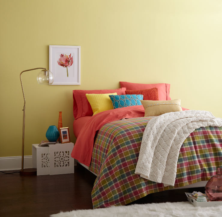 A bedroom with yellow walls. The bedding is coral, yellow and green.