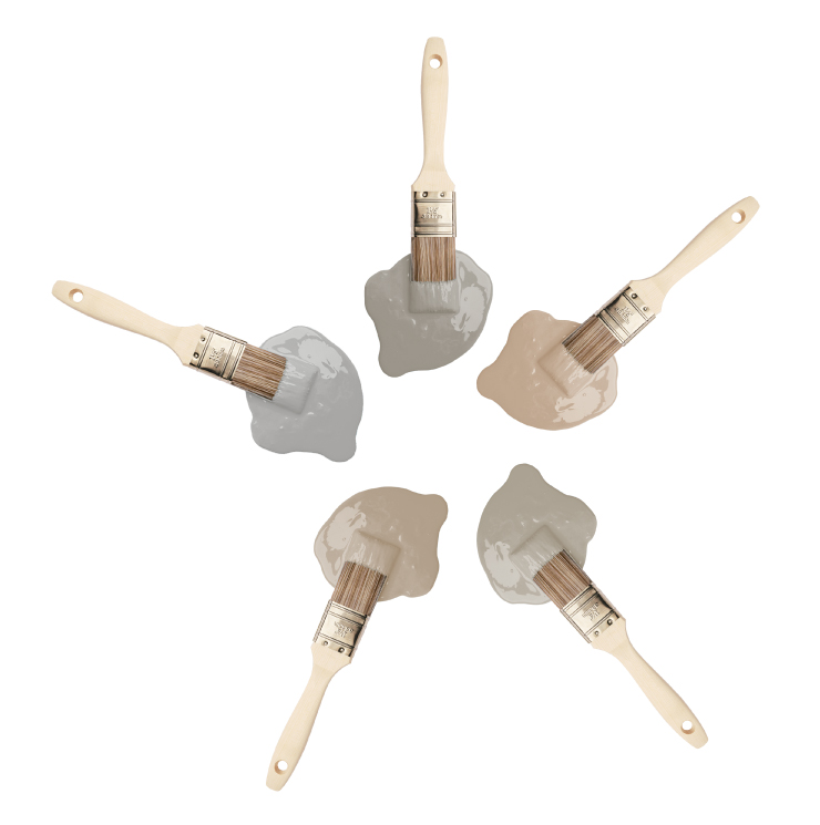 Five paint brushes dipped into paint drops that are beige and gray colors.